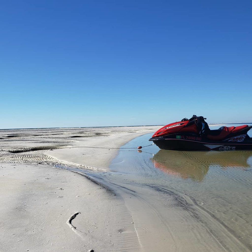 a red and black jet ski parked on the very shallow end of the beach at Crooked Island Beach in Florida
