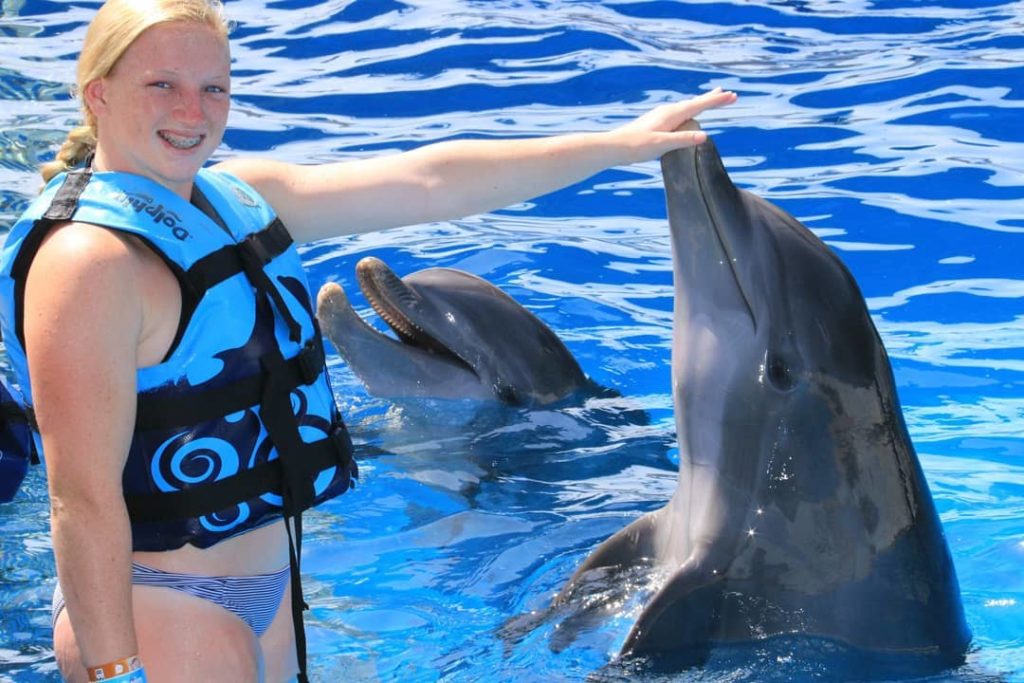 a girl smiling at the camera as she touches the dolphin