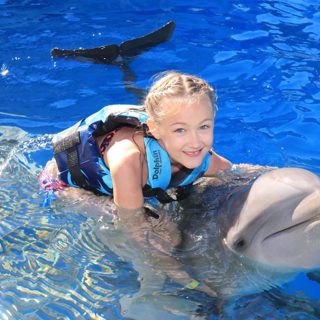 young girl with blue eyes holding on to dolphin in the water at Gulf Marine Park in Panama City Florida