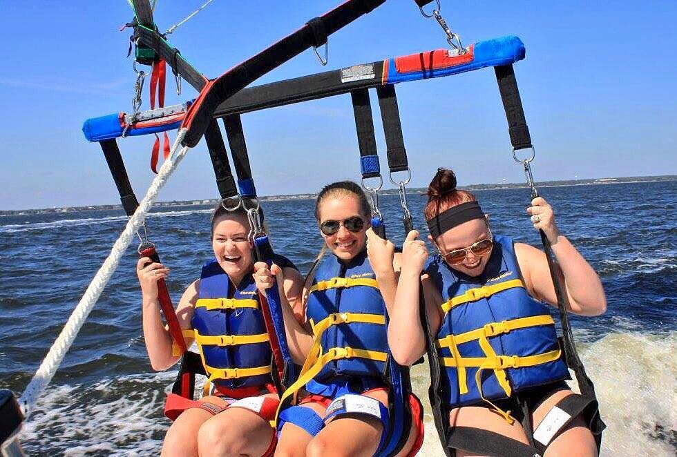 three girls smiling and laughing while they get ready to take off paragliding 