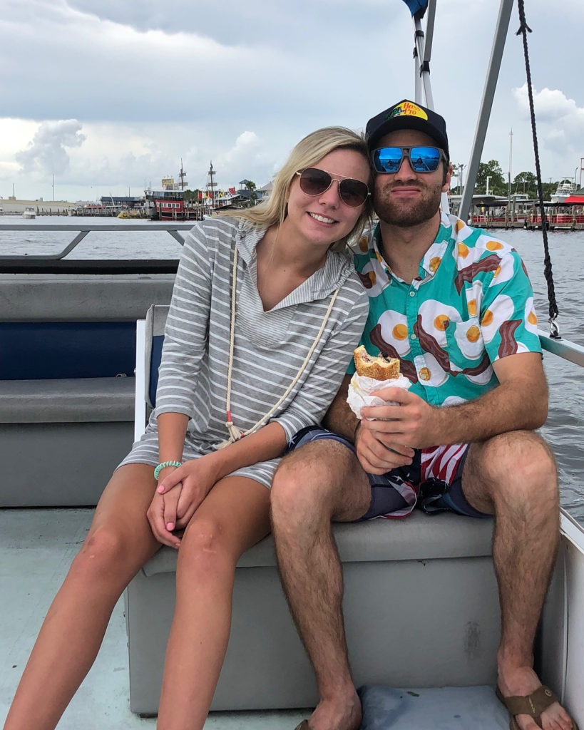 a man and a women sitting on a boat while the man is eating a sandwich 