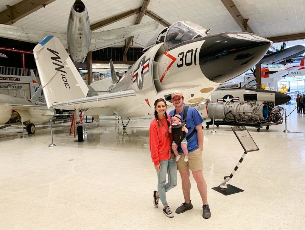 mom, dad and baby smile and pose in front of naval jet at the National Naval Aviation Museum 