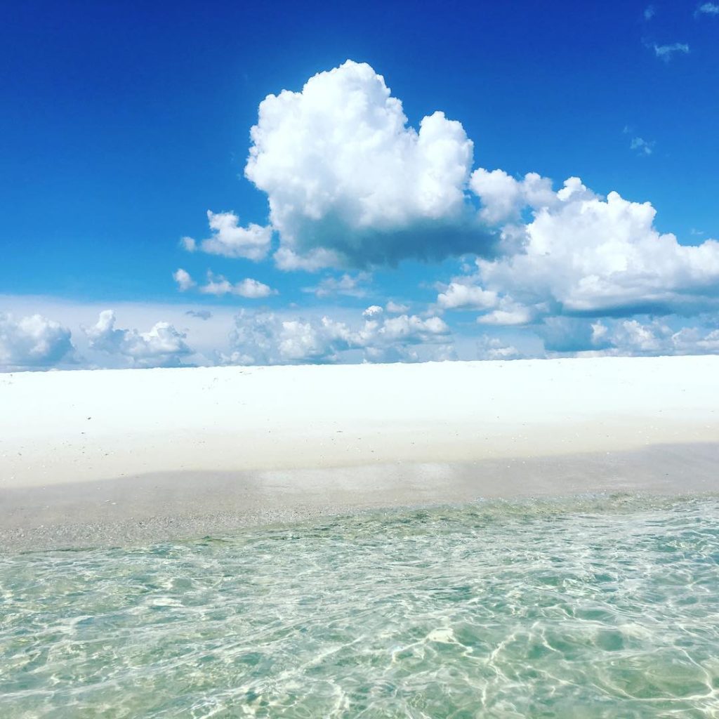 view of a white sanded empty beach from the clear water on a sunny day with bright blue skies and two big clouds