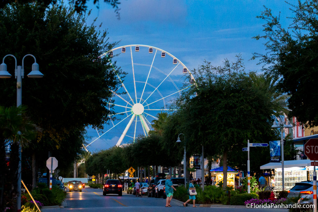 view of a ferris wheel from a small shopping town during the evening, pcb