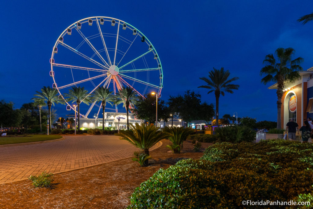 view of a giant ferris wheel lit up in different colors at night, pier park in panama city beach, florida