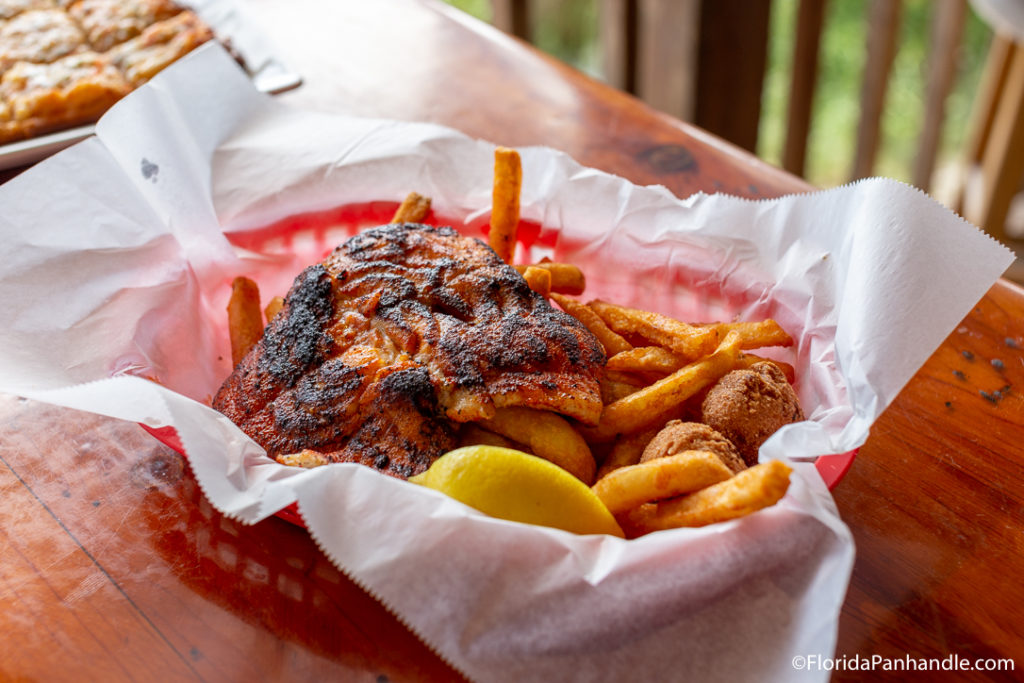 blacked and grilled fish on top of fries next to lemon in red basket