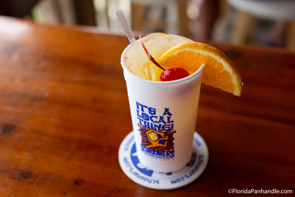a cocktail with a fresh slice of orange and a cherry on top in a white cup with blue lettering at Schooners Last Local Beach Club