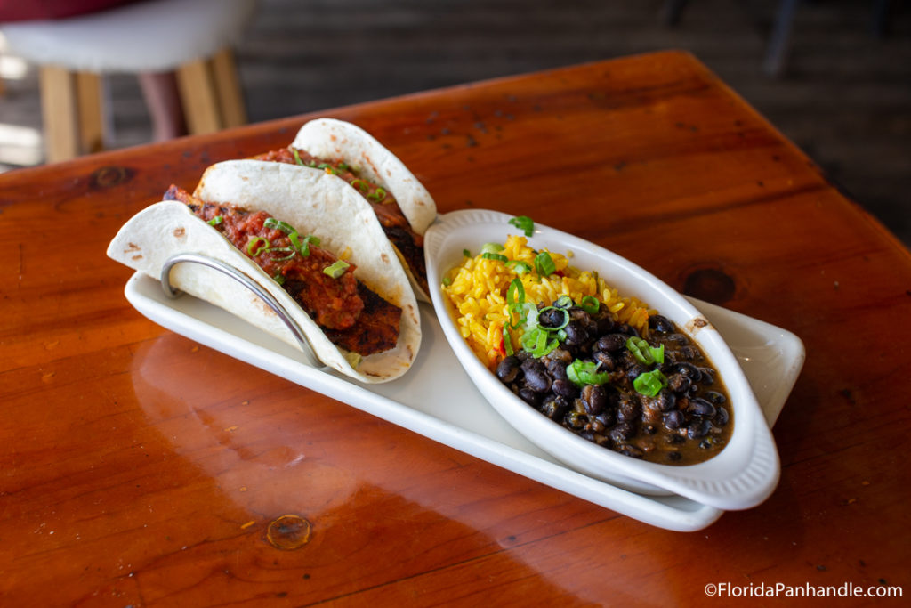 two tacos inside taco holder next to mexican rice and black beans
