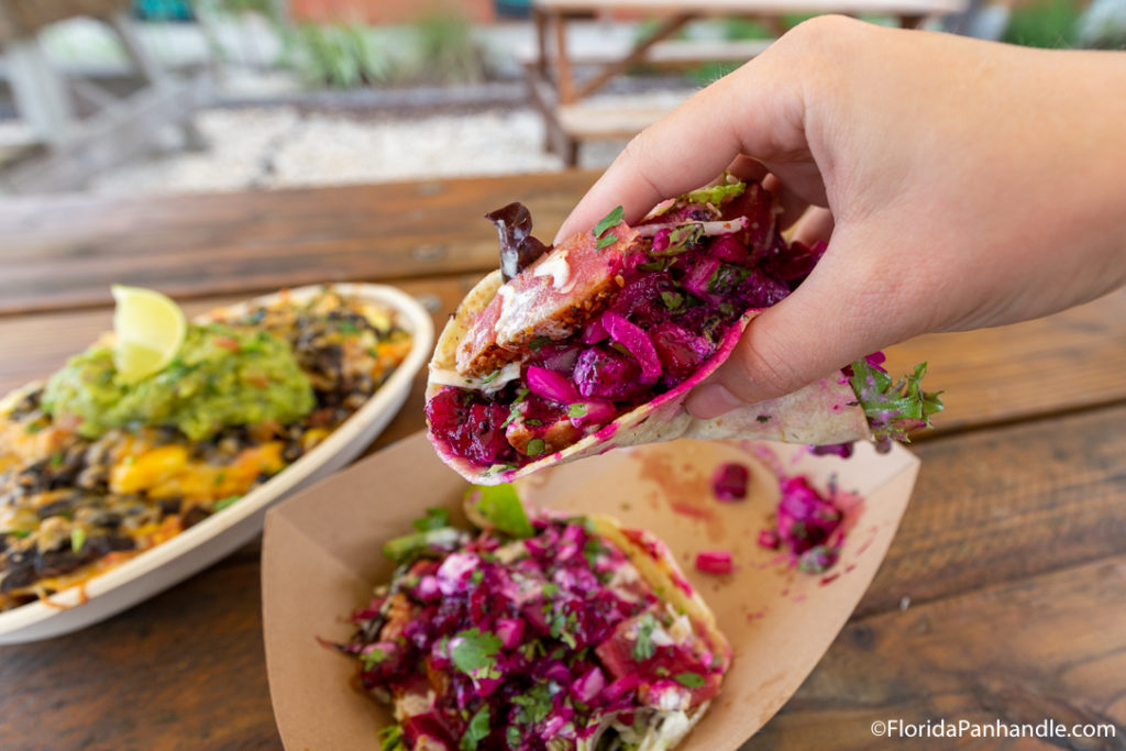 person holding taco with bright purple cabbage inside at finns island style grub