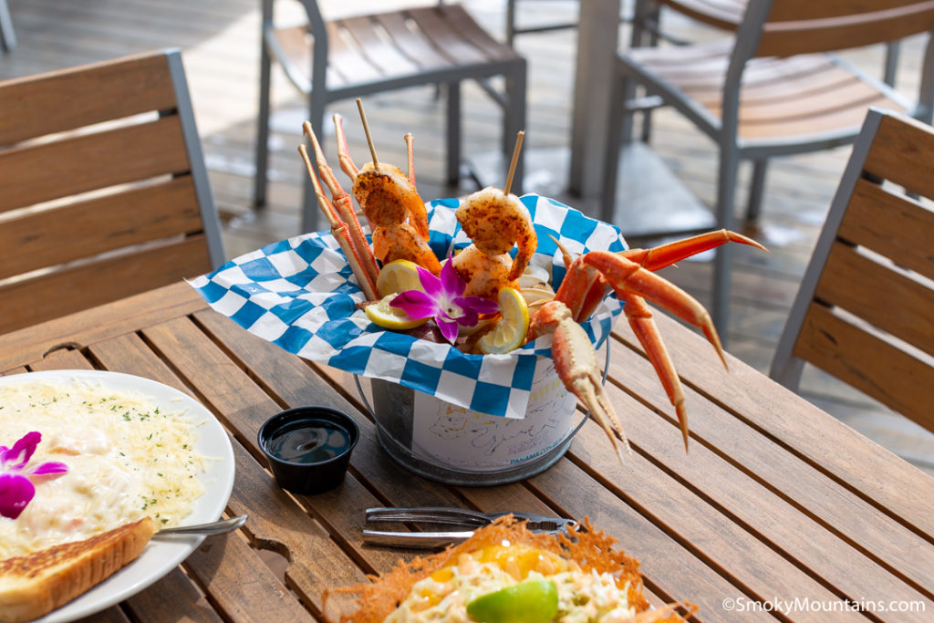 a tin bowl with blue and white checkered lining and shrimp skewers with crab legs poking out from the inside