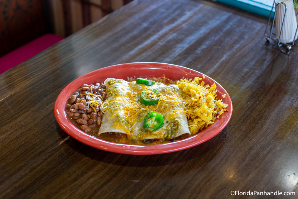 a plate of enchiladas with a side of yellow rice and beans 