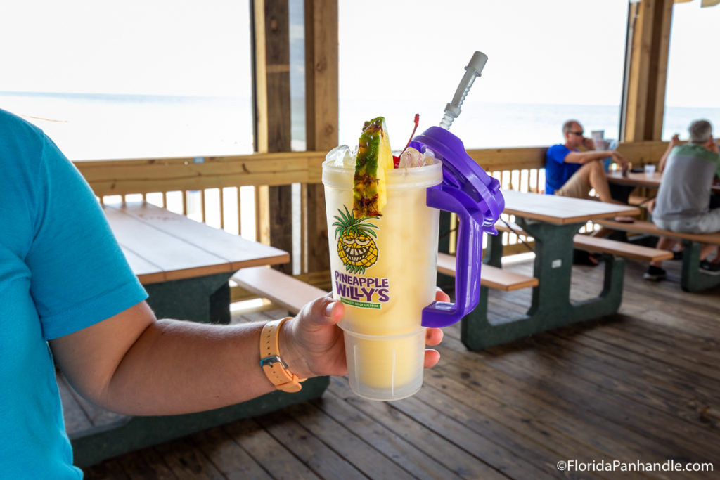 a person holding a tall plastic cup of pina colada with a fresh pineapple slice and a cherry on top at Pineapple Willy's