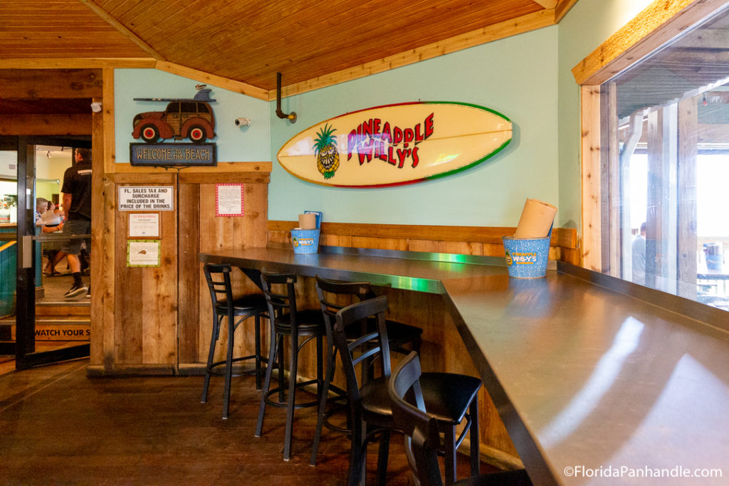 a hightop seating area with a surfboard that says pineapple willys on it at Pineapple Willies in Panama City Beach Florida