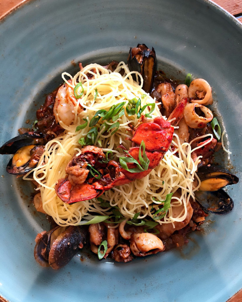 a plate of angel hair spaghetti on mussels and scallops with a small lobster tin and copped green onions on top at The Grand Marlin