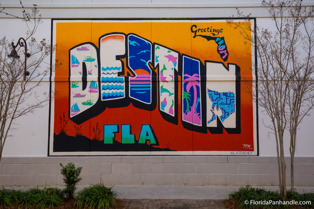 orange destin mural on the side of a building in between two trees