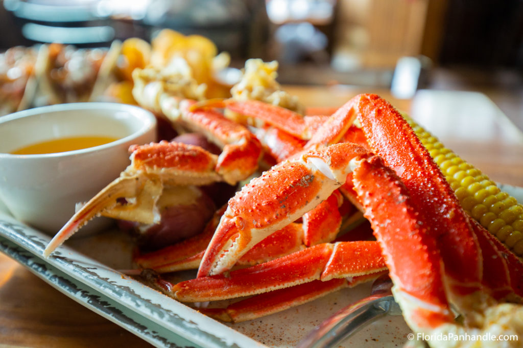 a plate of bright red boiled crab legs with a side of dipping butter and corn
