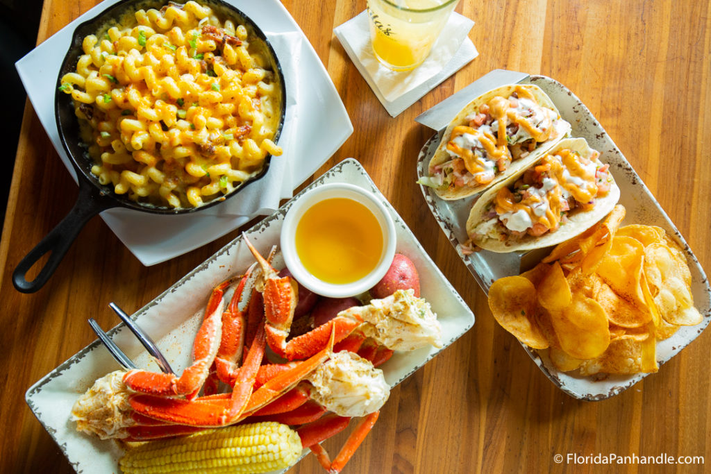 a plate of crab legs, a plate of bakes mac and cheese, and a plate of fish tacos with a side of chips