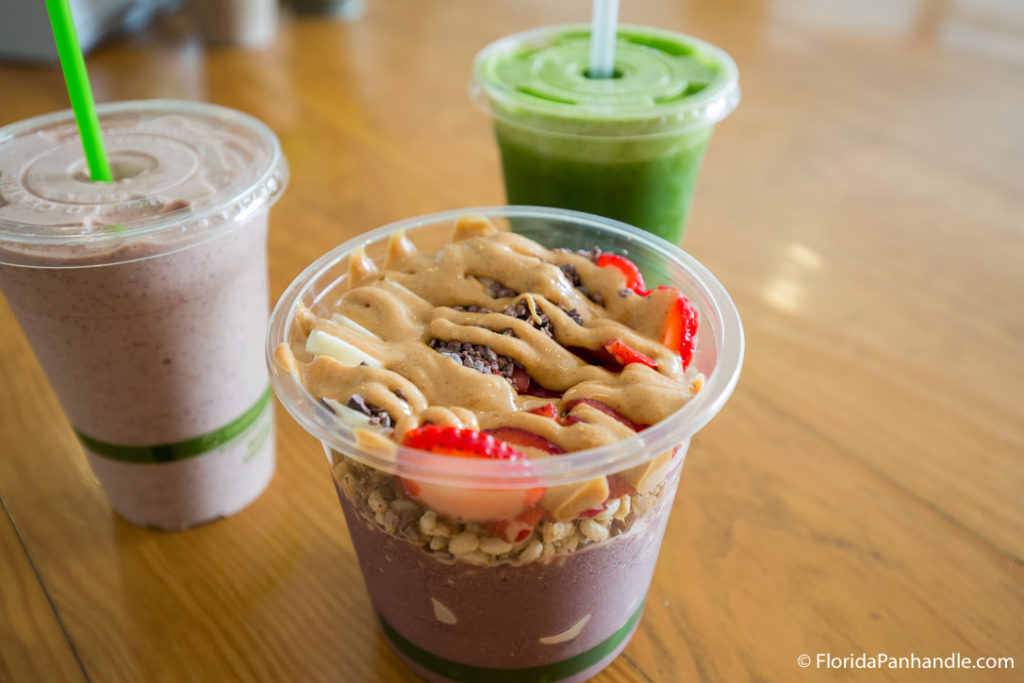 a smoothie bowl with granola, strawberries, blueberries and peanut butter in top with a green smoothie and purple smoothie on the side