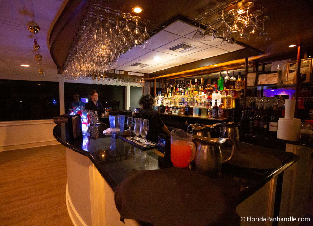 a bar with black marble counter tops and glasses hanging from the top