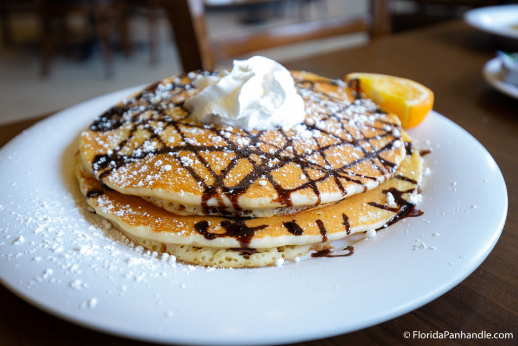 a stack of three pancakes with chocolate drizzle, powdered sugar, and whipped cream on top at the Pancakery