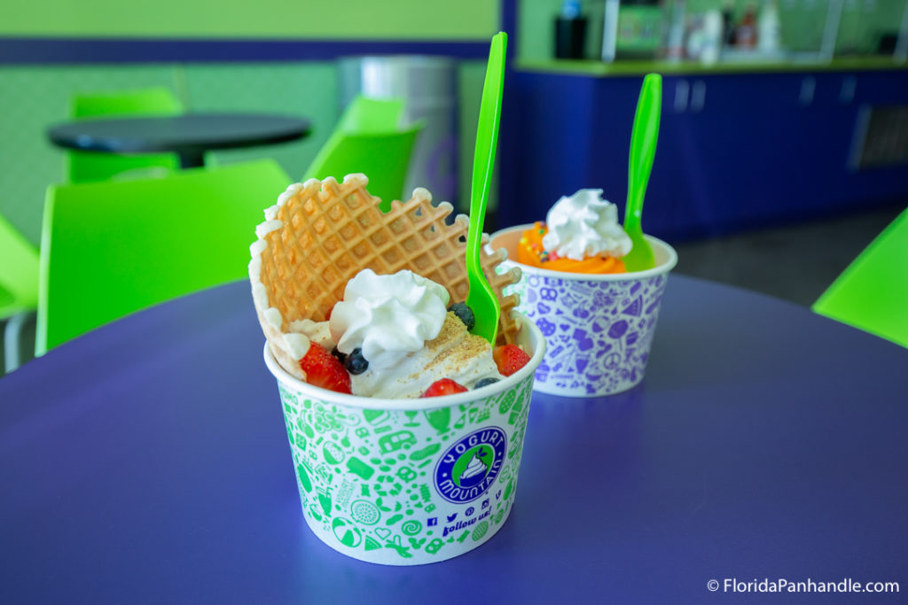 a cup of vanilla frozen yogurt with strawberries, whipped cream, and blueberries on top with half of a waffle cone on top at Yogurt Mountain