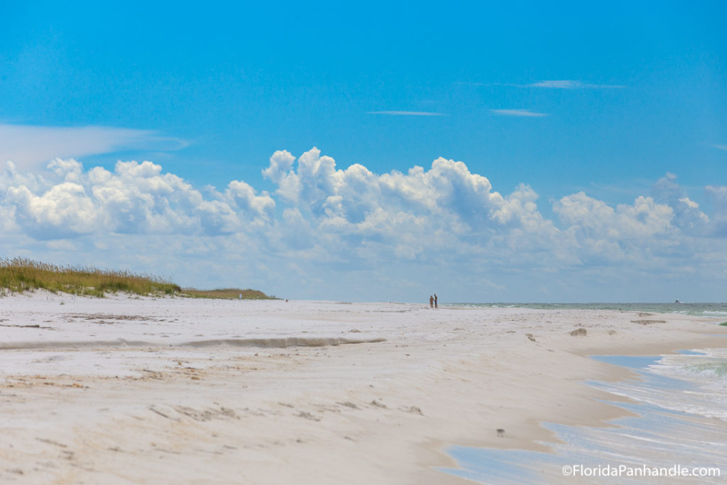 two people walking on the beach on a sunny day with blue skies in Panama City Beach