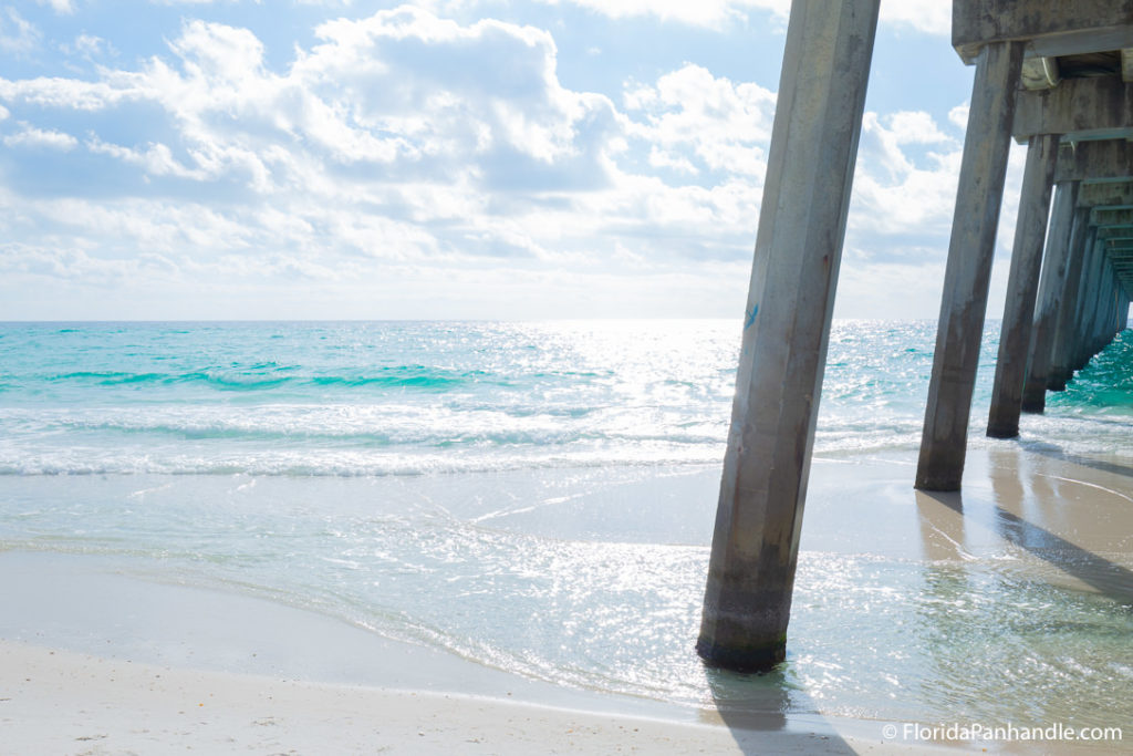 view of the beach from underneath the pier on a super sunny bright day at Pensacola Beach Gulf Pier in Florida, best beaches florida panhandle