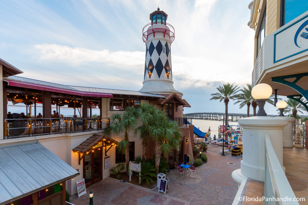 statue of a lighthouse on top of lit up outside second floor restaurant along side the beach in HarborWalk Village, destin free