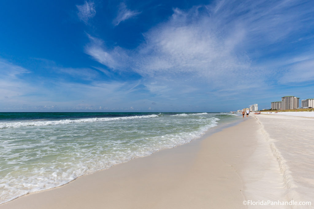 two people walking along the shoreline on a clear blue sky day at Henderson Beach State Park