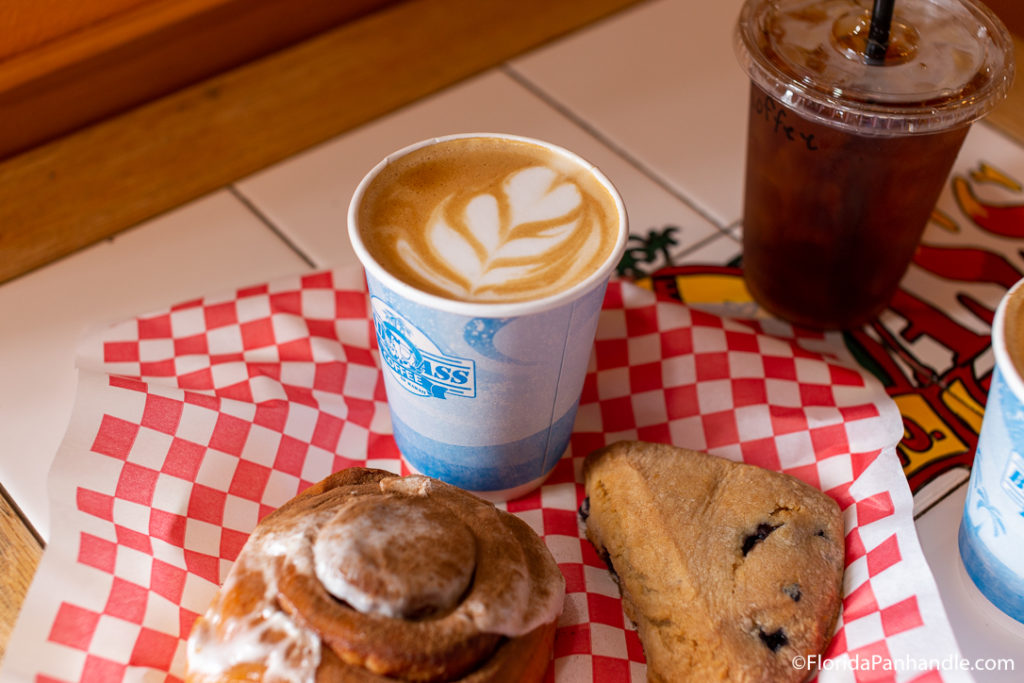 above view of scone and hot coffee with design in it on top of red and white checkered paper next to an iced coffee