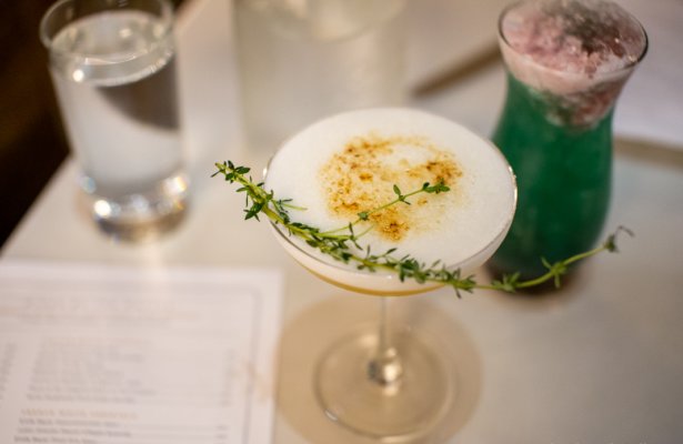 a cocktail with white foam on top and a string of thyme