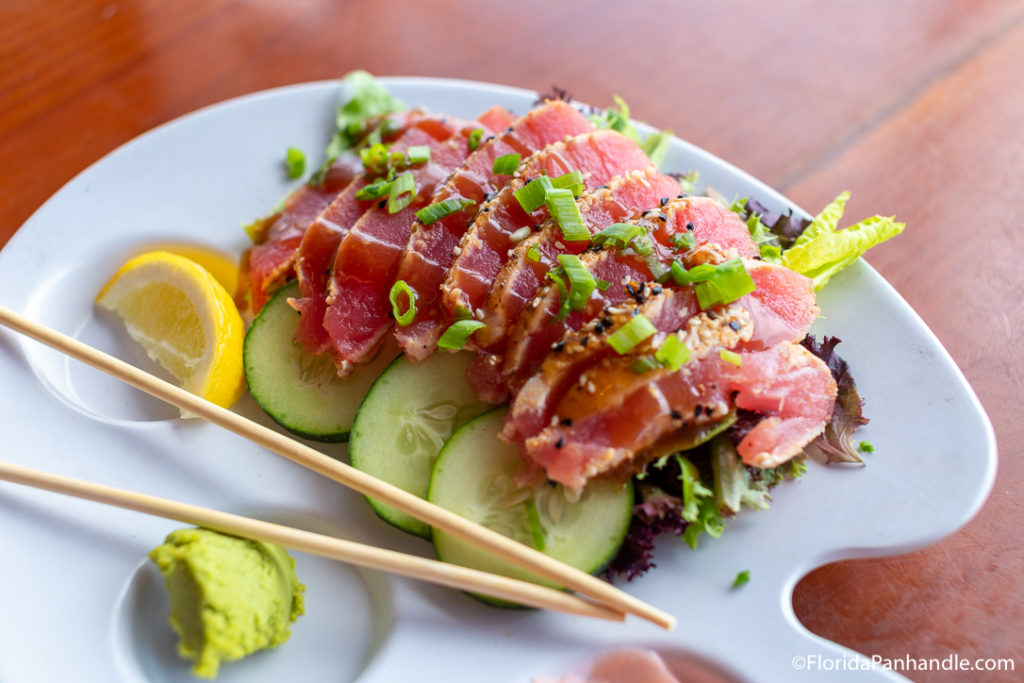 a plate of raw tuna on a bed of salad with a slice of lemon on the side