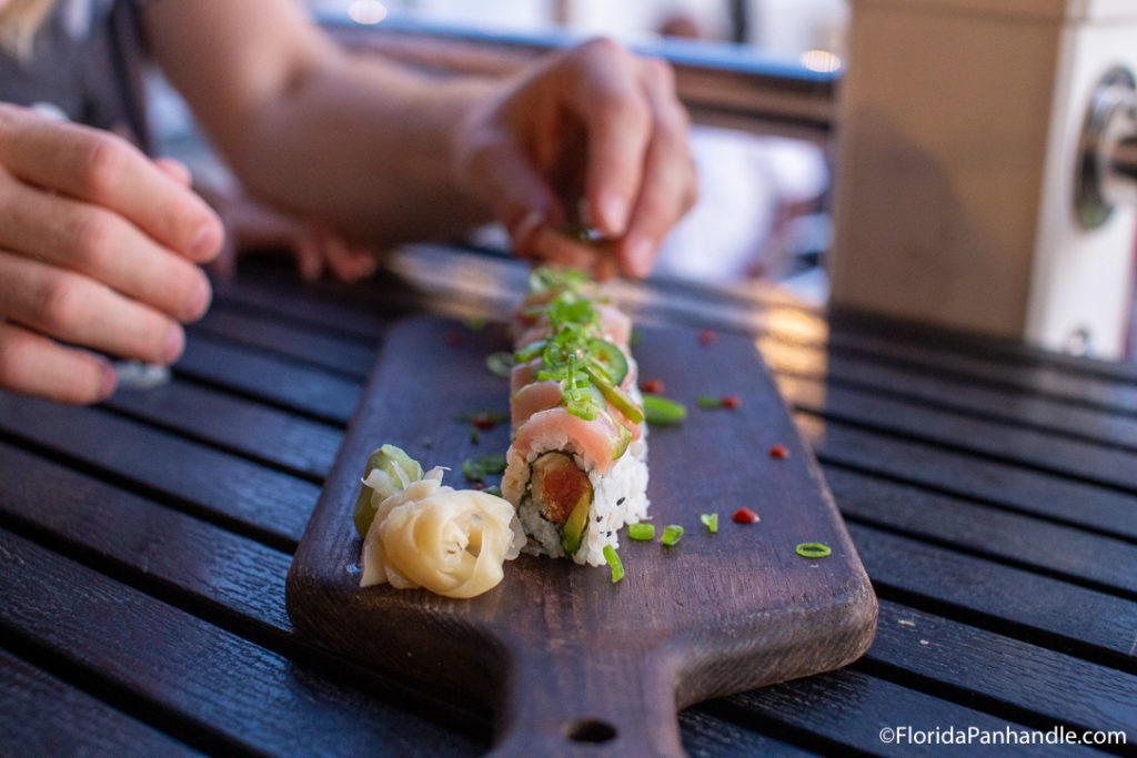 a wooden pallet with a sushi roll on top with a side of ginger and wasabi