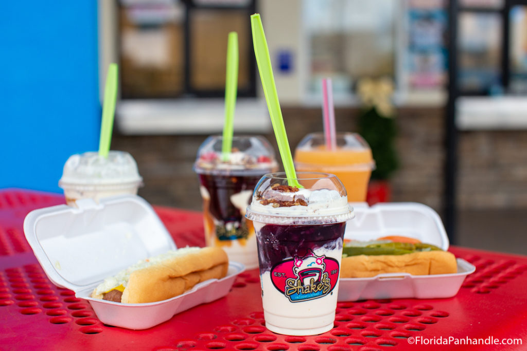 a vanilla and fudge milkshake next to two hot dogs in styrofoam containers at Shake's Frozen Custard