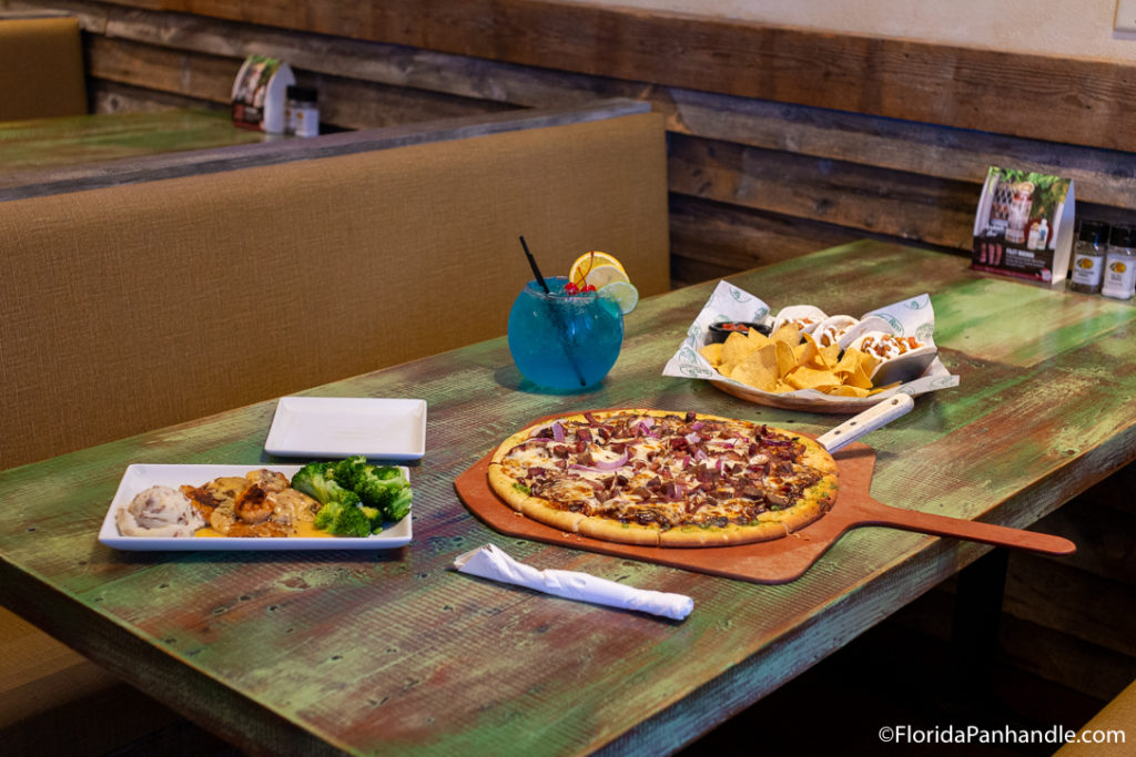 a dining booth with pizza, chips and salsa, and a blue drink on it