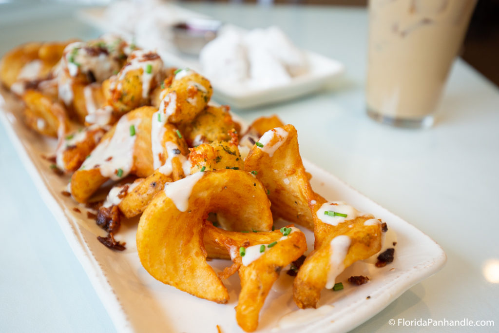 a plate of crispy potatoes with white sauce drizzle and herbs on top