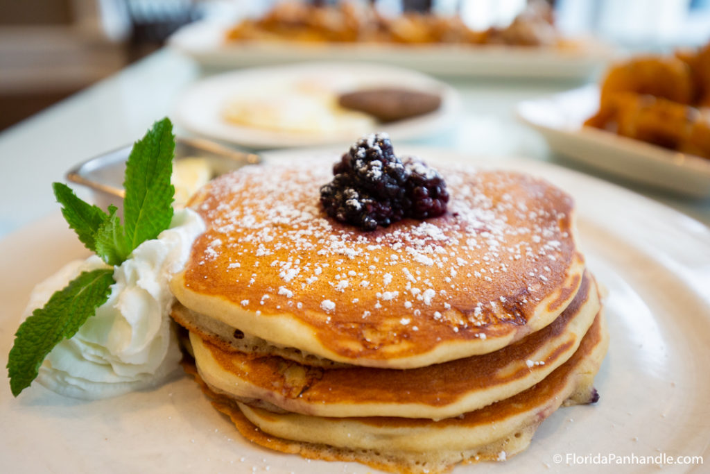 a stack of pancakes with a dollop of blackberries on top with whipped cream and basil on the side