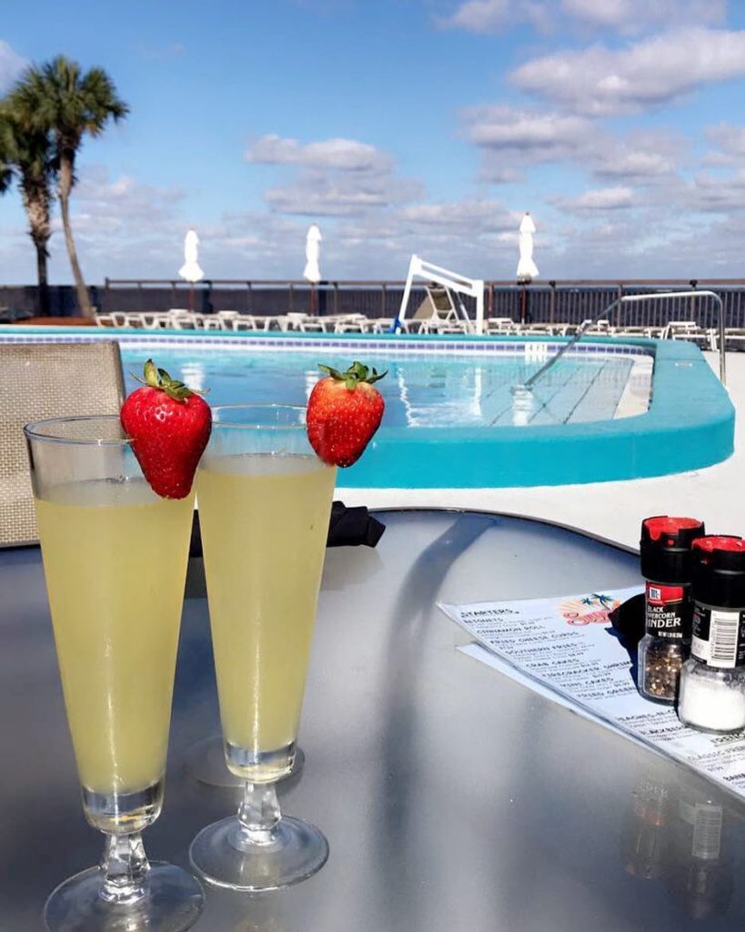 two cocktails with a fresh strawberry stuck on the rim on s table by the pool