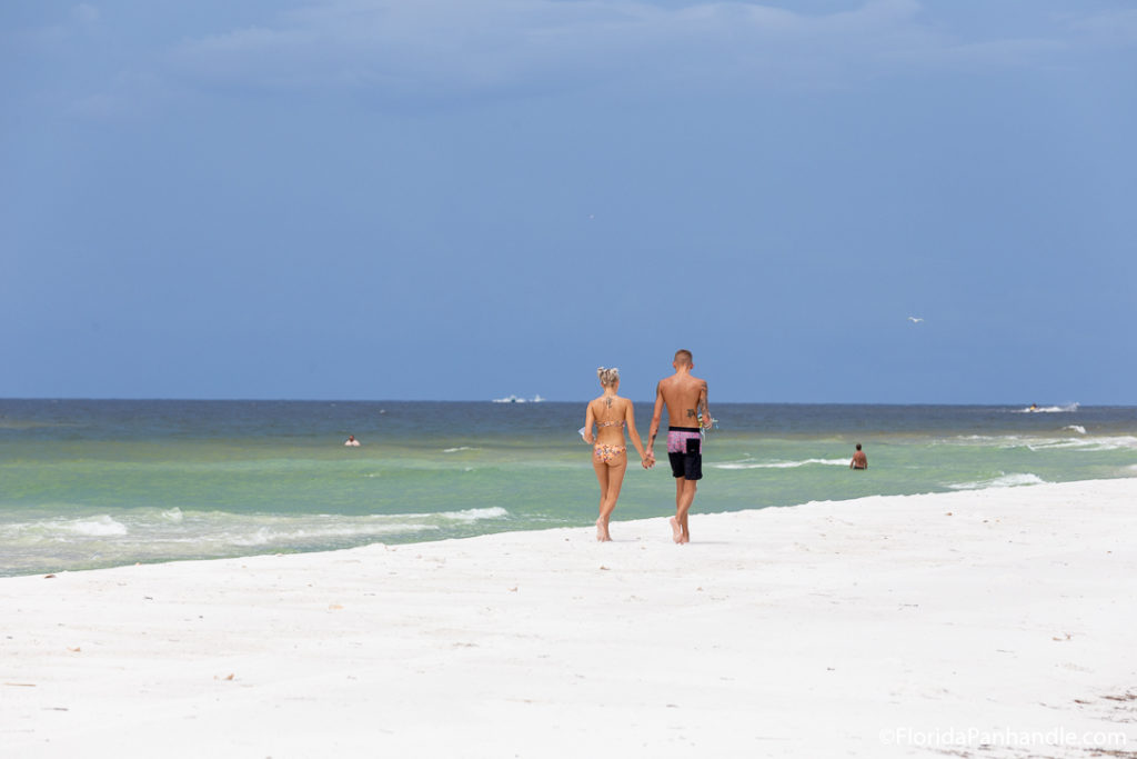 a couple walking along the shoreline of the beach holding hands during the day 