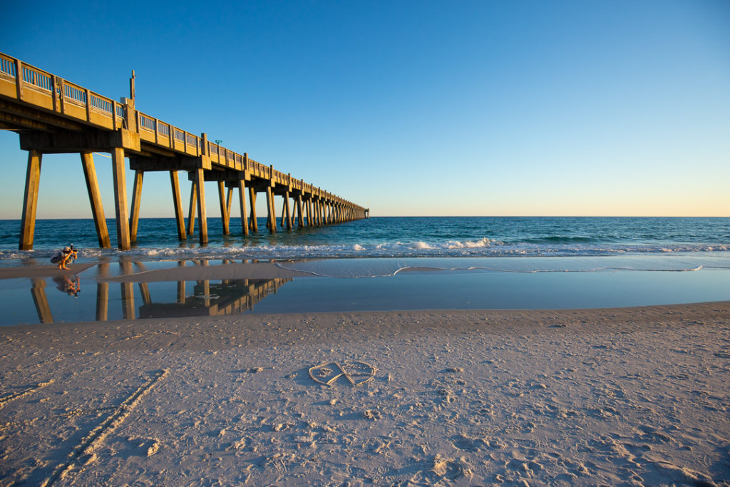 view of boardwalk and the ocean with some drawings in the sand and the water washing away from the shore during sunset at Casino Beach