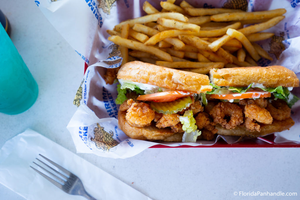 a deep fried shrimp sandwich with lettuce tomatoes and pickles and a side of fries at Shrimp Basket