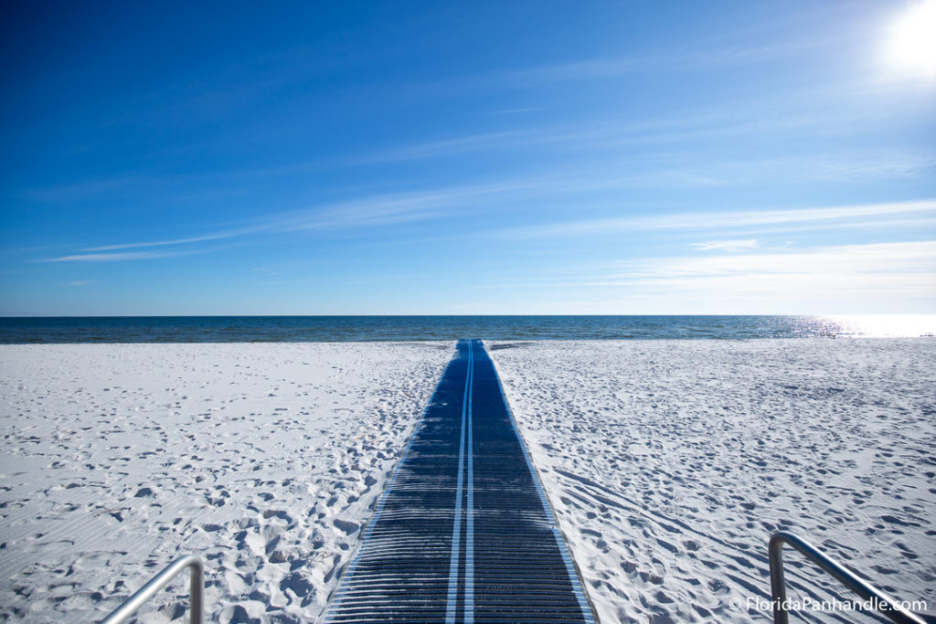 a straight black road to the oceanfront with sand on either side at a Pensacola Beach called Langdon Beach