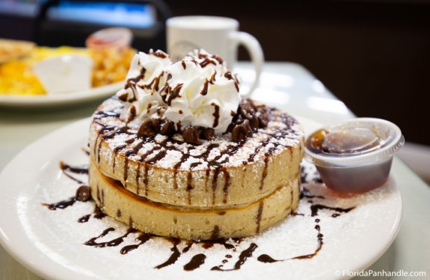 a stack of thick fluffy pancakes, with chocolate chips, whipped cream and powdered sugar on top