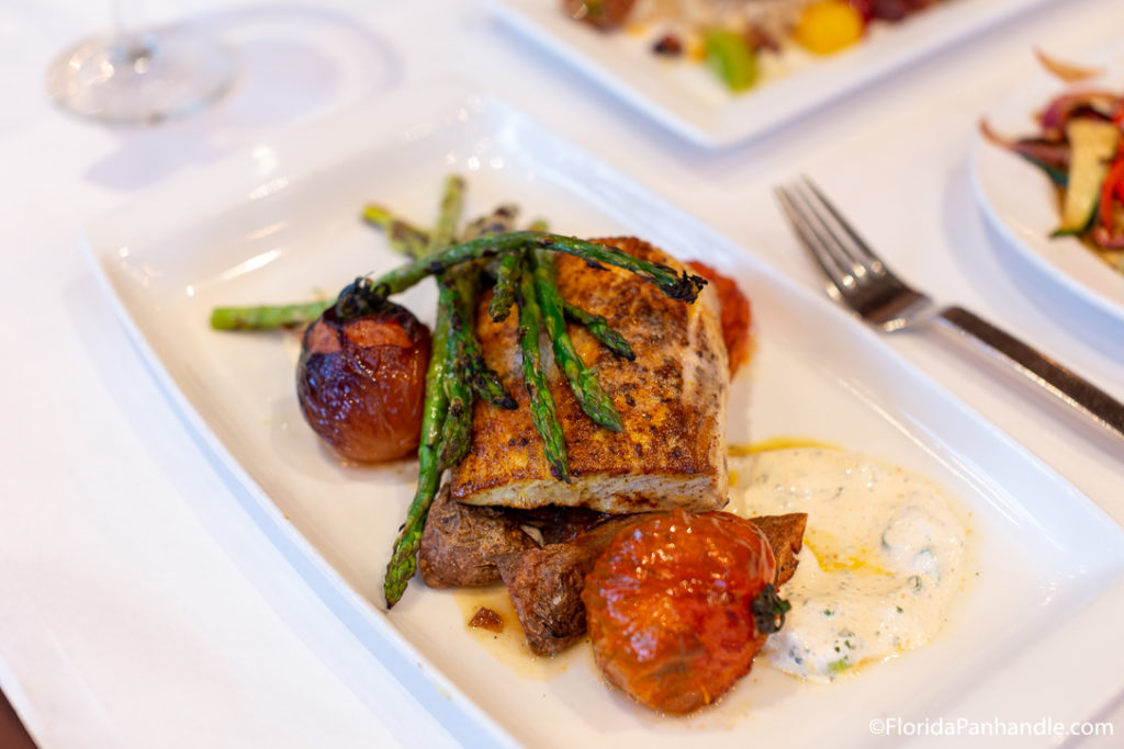 a plate of grilled fish with diced potatoes and asparagus and blistered tomatoes