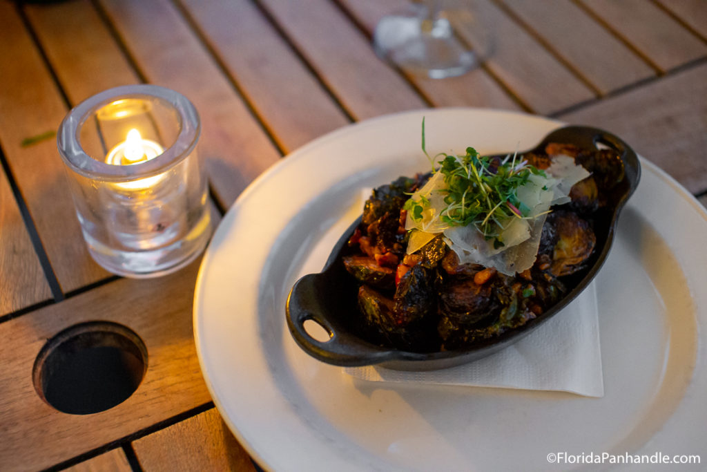 dish filled with caramelized Brussels sprouts with shredded cheese on top next to a candle light at The Grand Marlin 