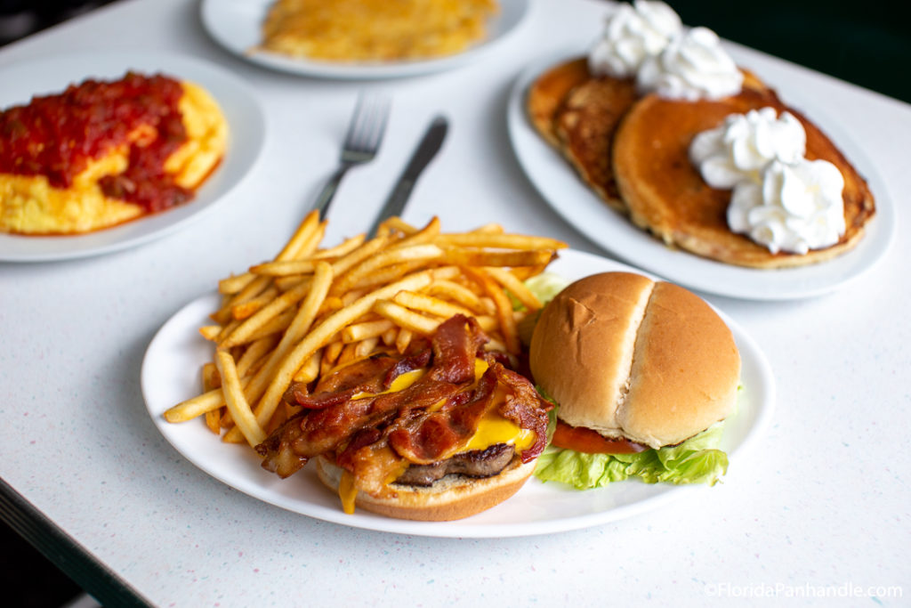 plate of hamburger with a side of fries  next to a plate of pancakes with whipped cream on top at All American Diner