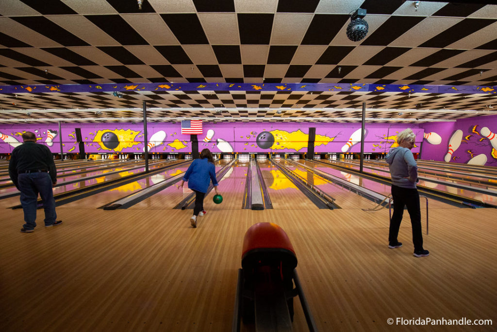 people bowling at Rock'it Lanes with checkered ceilings and purple painted background with bowling balls and pins