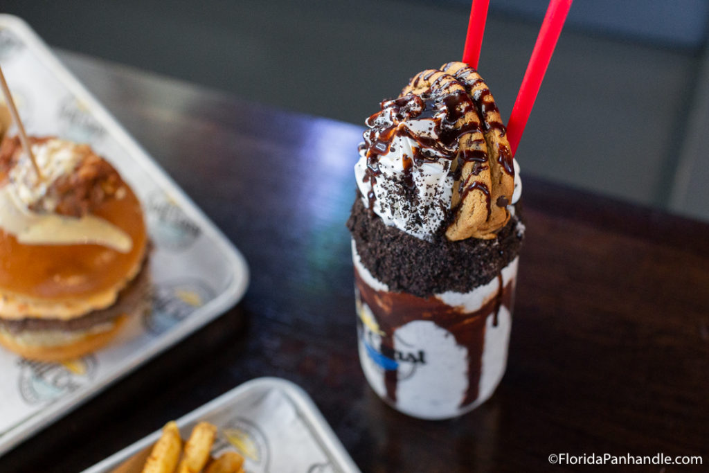  chocolatey milkshake rimmed with crushed oreos and topped with whipped cream, two chocolate chip cookies and chocolate syrup at Gulf Coast Burger Company