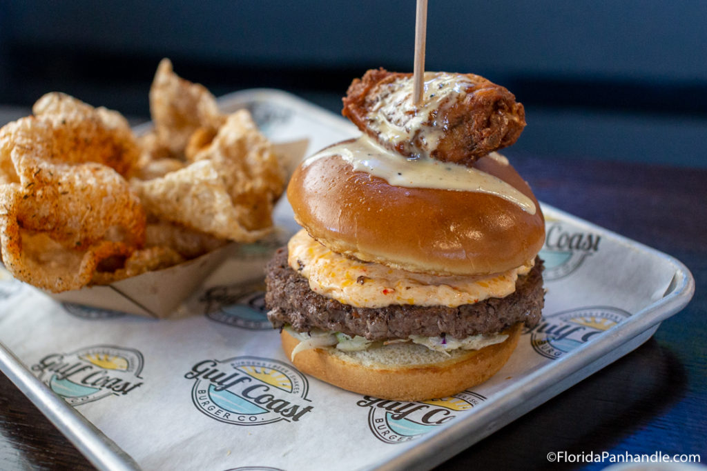a saucy burger with a chicken wing on top and a skewer through it with a side of fried pig fat