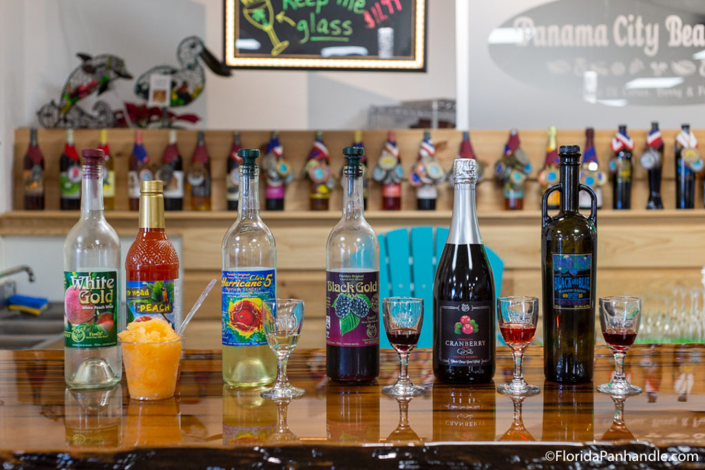 white, red, yellow, blue and purple wine with sample glasses in front at Panama City Beach Winery